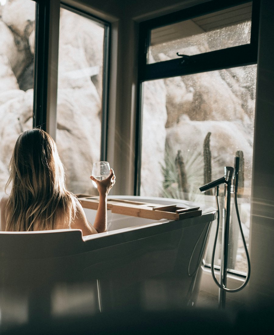 Femme se détendant dans un bain face à une grande fenêtre