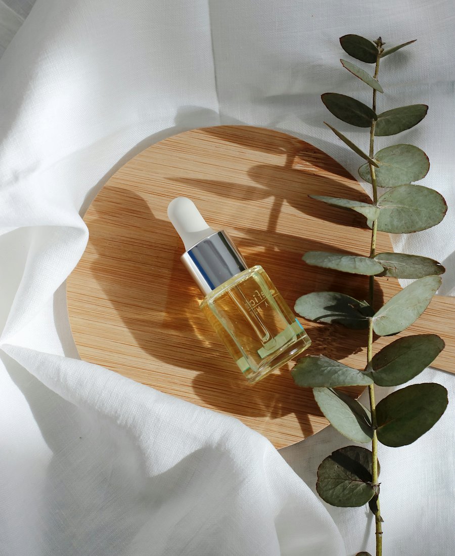Flacon de sérum posé sur un plateau en bois, branches d’eucalyptus